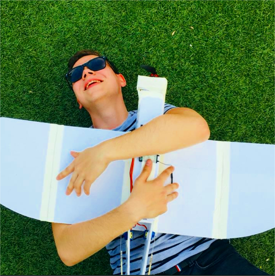 A person lying on the grass holding a large model airplane